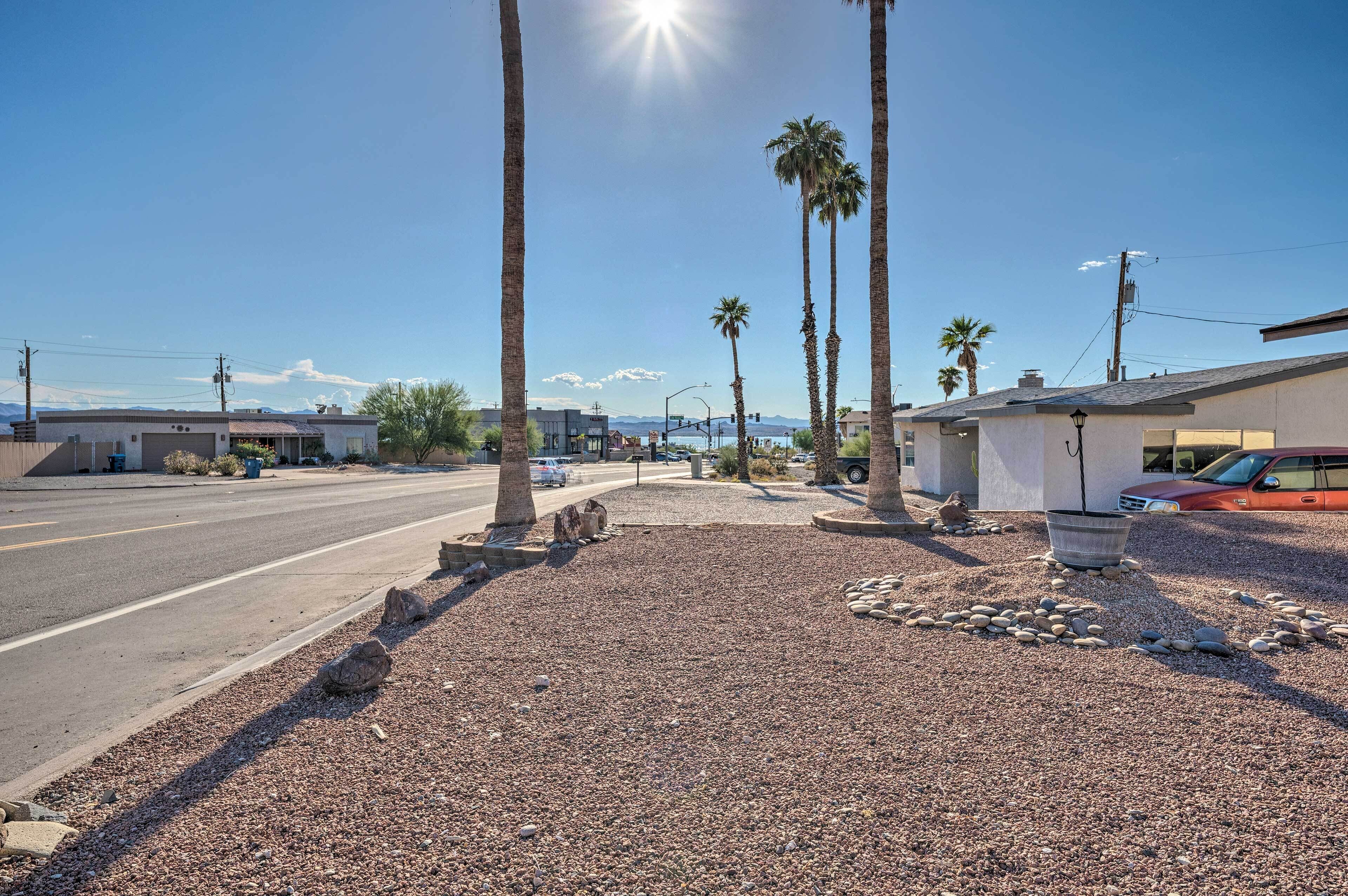 A street with palm trees, a gravel area, and a building with a garage.