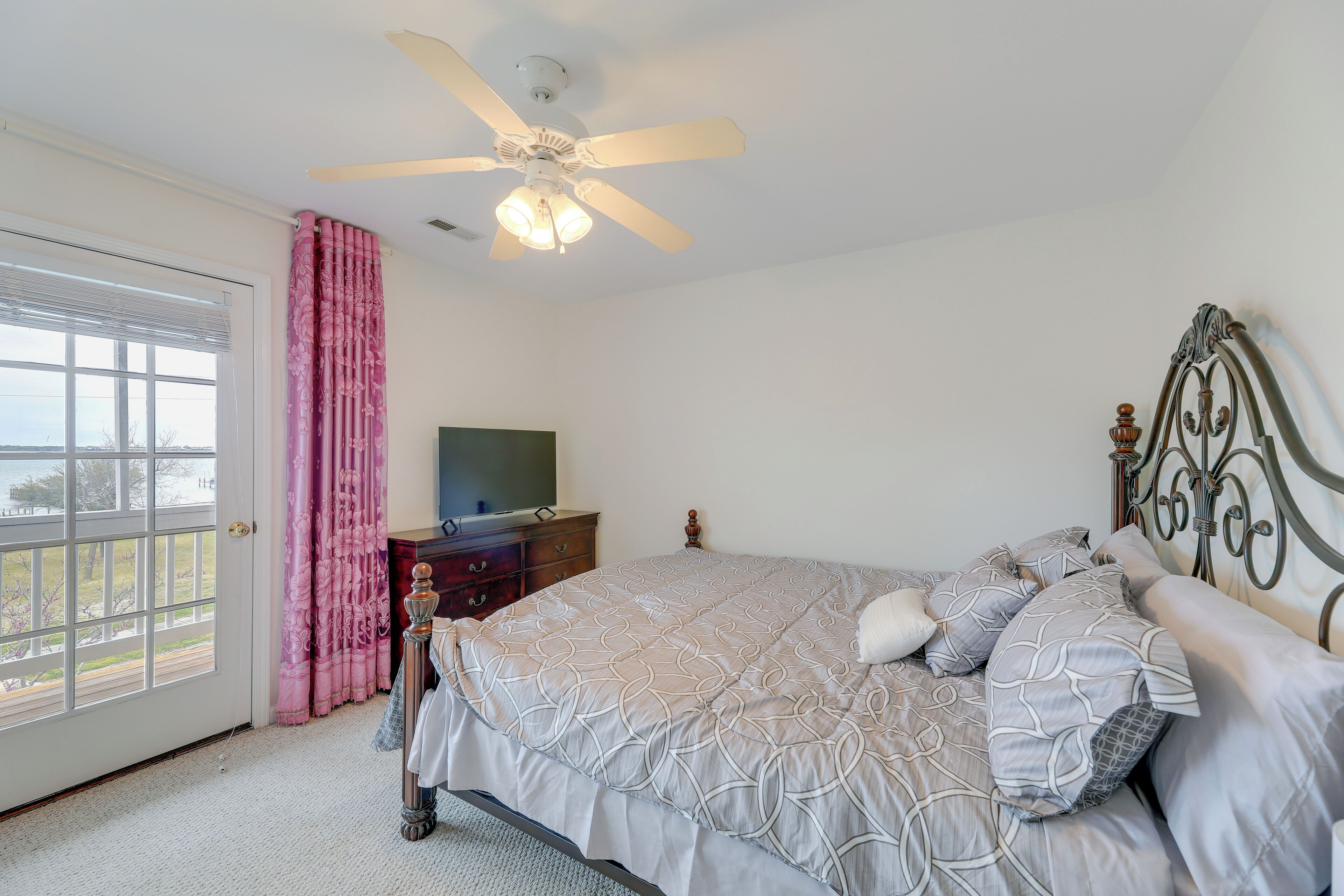 Une chambre à coucher avec un lit, un ventilateur de plafond, une commode et une fenêtre avec des rideaux.