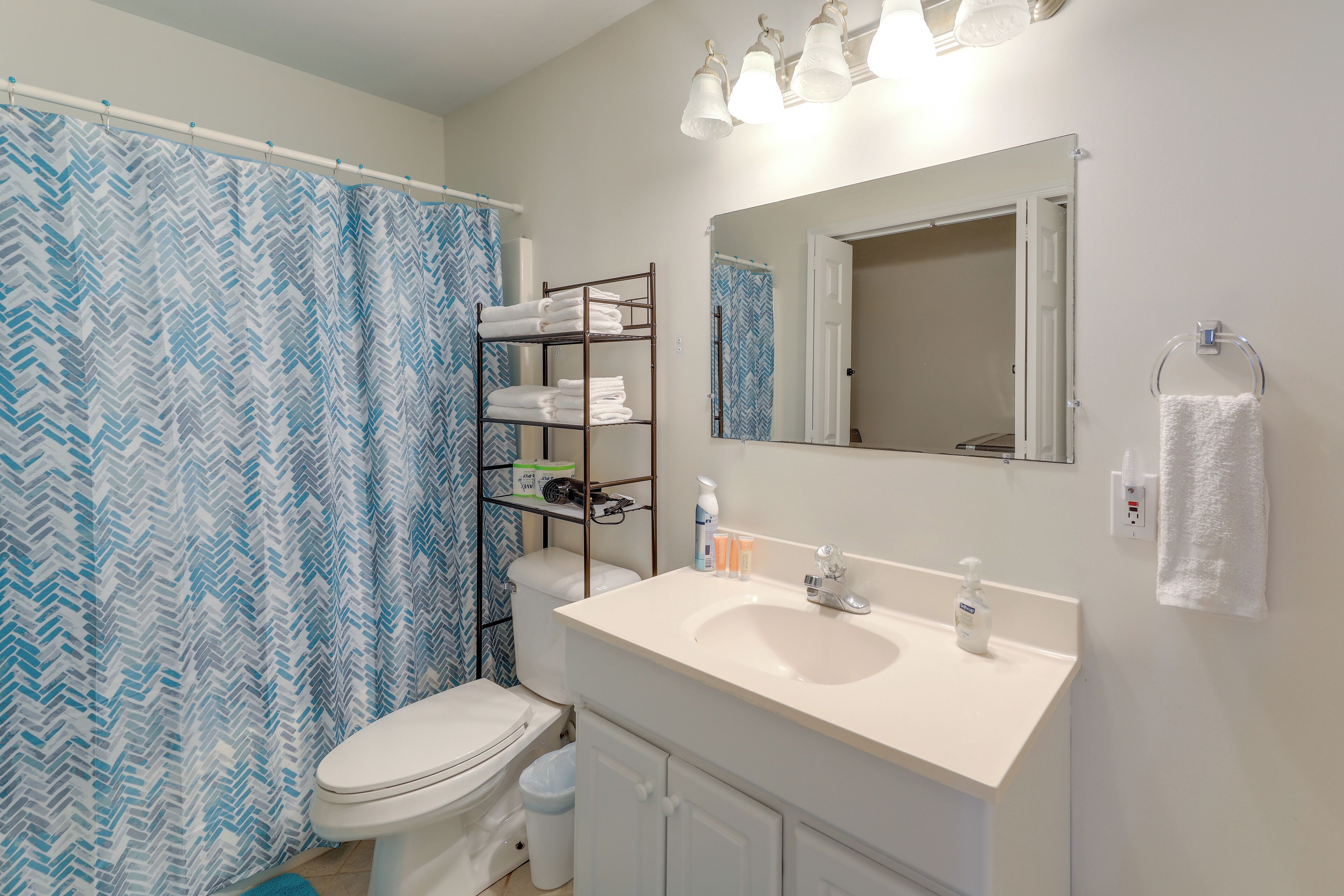 Une salle de bain avec un lavabo blanc, un miroir, un porte-serviettes et un rideau de douche.