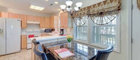 A modern kitchen with a marble countertop, wooden cabinets, and a dining area with a table and chairs.