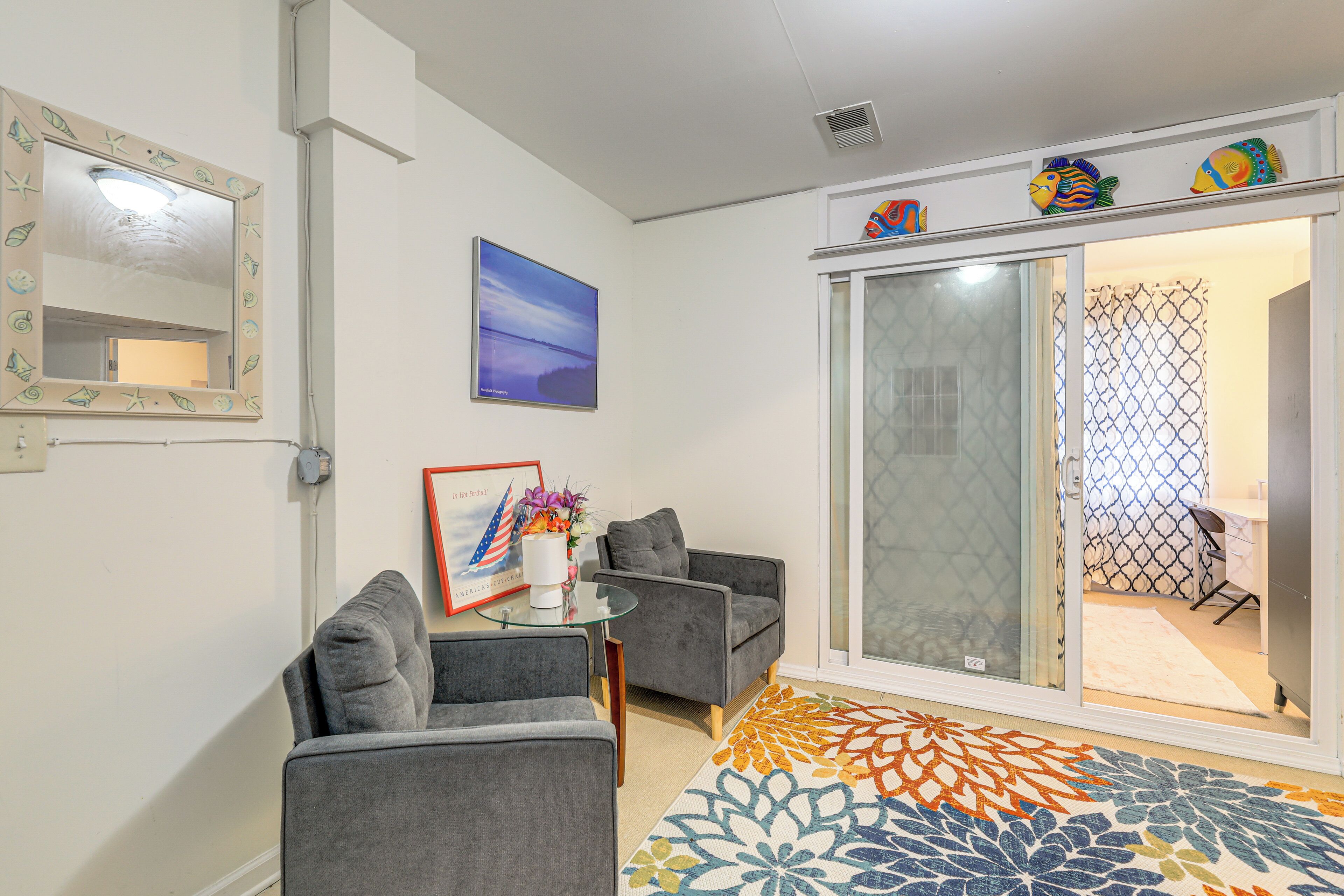 A living room with grey sofas, a glass coffee table, a framed picture, and a colorful rug.
