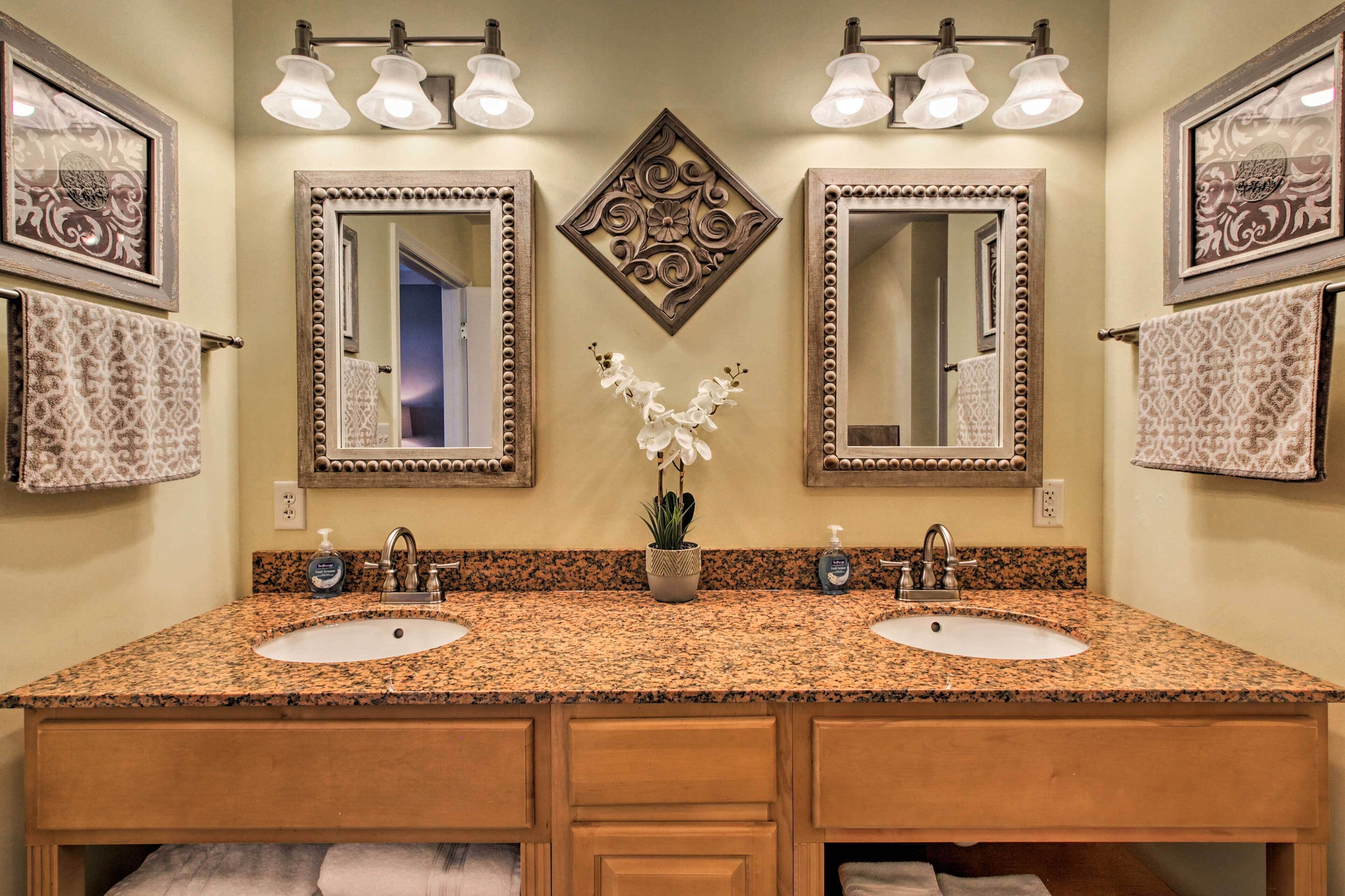 Un baño con dos lavamanos, encimera de granito y espejo decorativo con diseño floral.