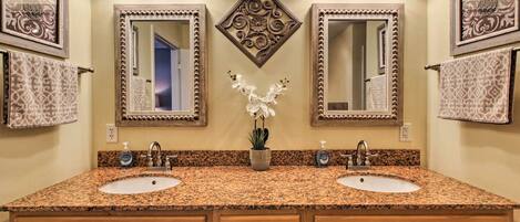 Un baño con dos lavamanos, encimera de granito y espejo decorativo con diseño floral.