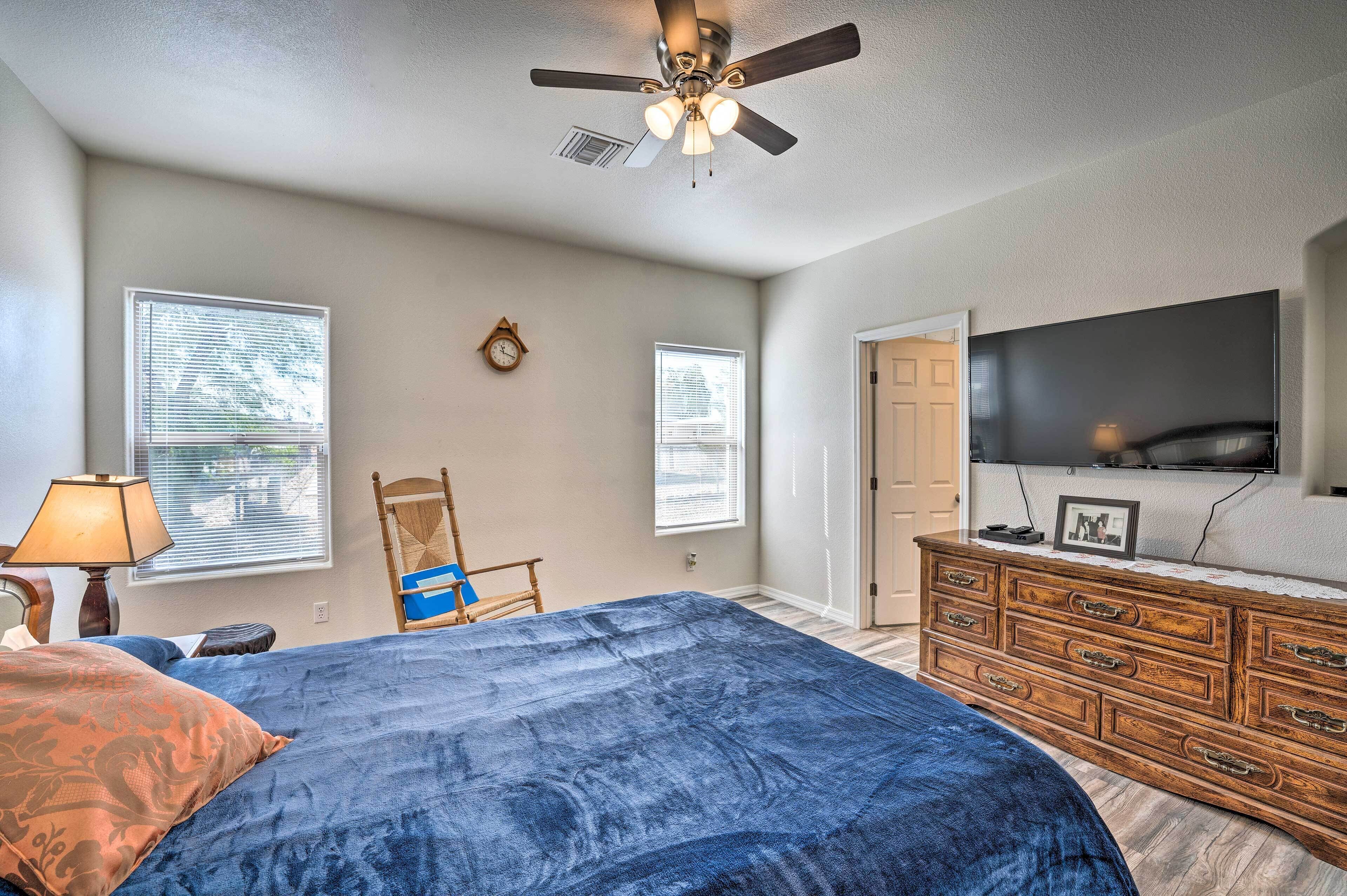 A bedroom with a bed, dresser, TV, and ceiling fan.