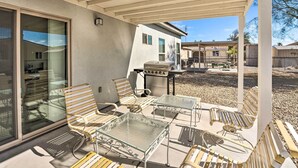 Une terrasse couverte, aménagée avec du mobilier d’extérieur, un barbecue et offrant une vue sur les maisons voisines.