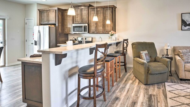 Une cuisine moderne avec des meubles en bois, un îlot central doté de tabourets, un four à micro-ondes et un réfrigérateur.