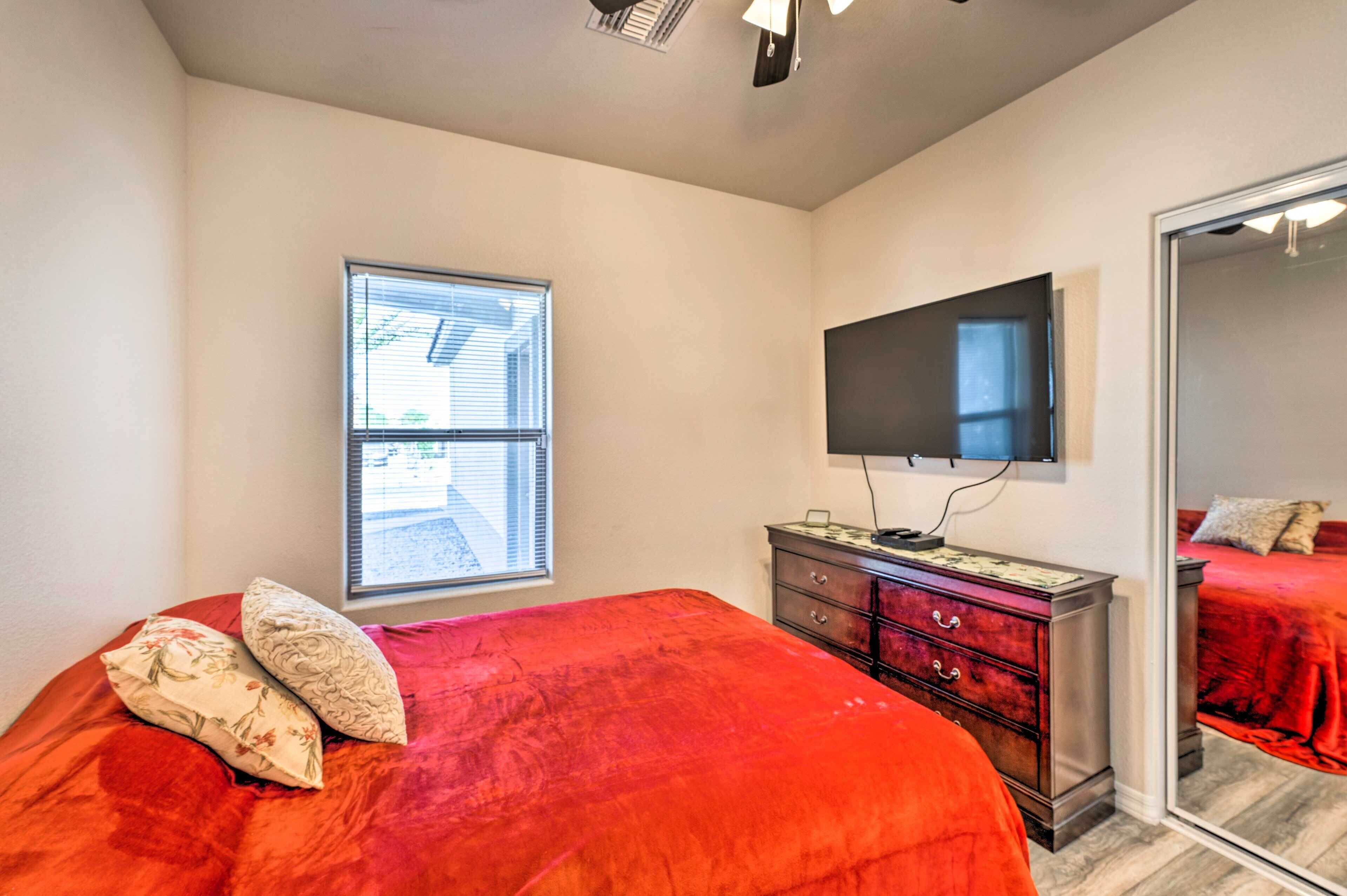 Une chambre à coucher comprenant un lit, une commode, un téléviseur fixé au mur et une fenêtre avec des stores.