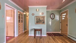 A hallway with wooden flooring, a small table, a painting, and a mirror on the wall. - Nostalgic & Retro Anaconda Home, Walk to Town (Anaconda)