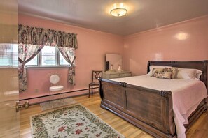 Een slaapkamer met een houten bed, een stoel, een kastje en een raam met gordijnen.