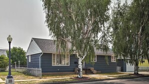 A residential house with a dark blue exterior, a sloped roof, and a front yard with a tree and a street lamp. - Nostalgic & Retro Anaconda Home, Walk to Town (Anaconda)