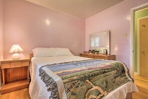 Een slaapkamer met een bed, nachtkastje met lamp, een dressoir en een spiegel.
