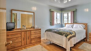 A bedroom with a wooden dresser, a bed with a quilt, a television on the dresser, and a window with curtains. - Nostalgic & Retro Anaconda Home, Walk to Town (Anaconda)