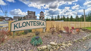 Een houten bord met de naam 'Klonteska' in een landelijke omgeving, met een houten hek, bomen en een bewolkte lucht.