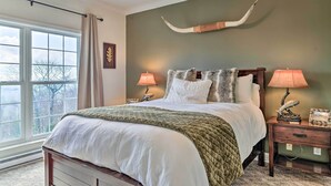 Een slaapkamer met een groot bed, twee bedlampen, een houten nachtkastje en een op de muur bevestigd hert.