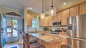 Een keuken met houten kastjes, roestvrijstalen apparatuur, een granieten werkblad en hangende lampen.
