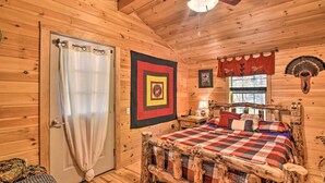 Un dormitorio de cabaña acogedor, con cama de madera, ventilador de techo, ventana con persianas y puerta con cortina.
