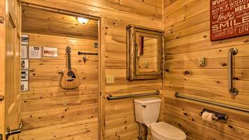 A wooden cabin bathroom with a toilet, a guitar, and a mirror.