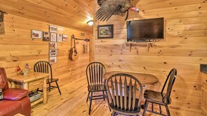 Interior de una cabaña de madera con un pavo colgado, cuadros enmarcados, una guitarra y un televisor.