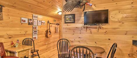 Interior de una cabaña de madera con un pavo colgado, cuadros enmarcados, una guitarra y un televisor.