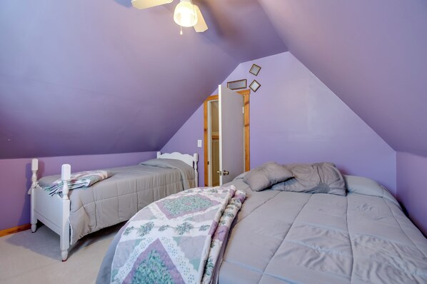 Une chambre avec deux lits, un ventilateur de plafond et une porte donnant sur une autre pièce.