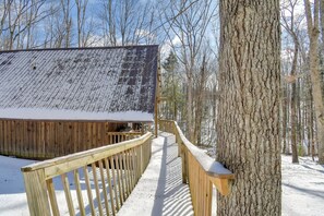 Une cabane en bois, dont le toit est recouvert de neige, entourée d’arbres dans une forêt enneigée.