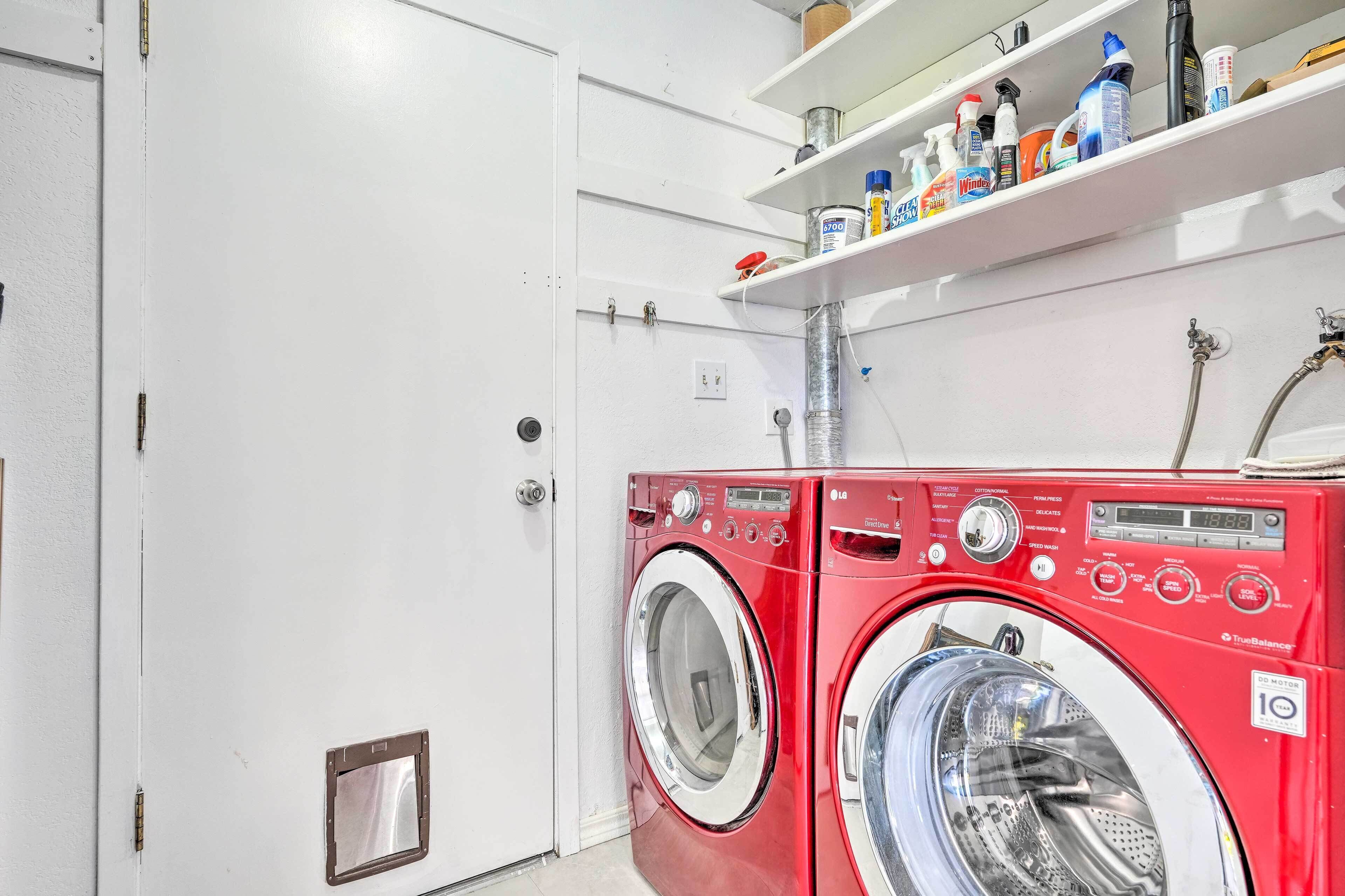 A red washing machine with a digital display, a white door, and a shelf with cleaning supplies.