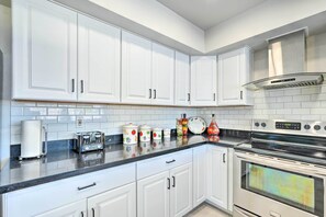 A kitchen with white cabinets, a black countertop, a stainless steel stove, and a tiled backsplash. - Spacious Home w/ Pool & Grill in Phoenix! (Phoenix)