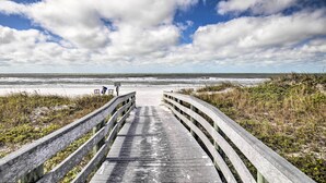Une promenade en bois qui mène à une plage d’où l’on a une vue dégagée sur l’océan et le ciel.