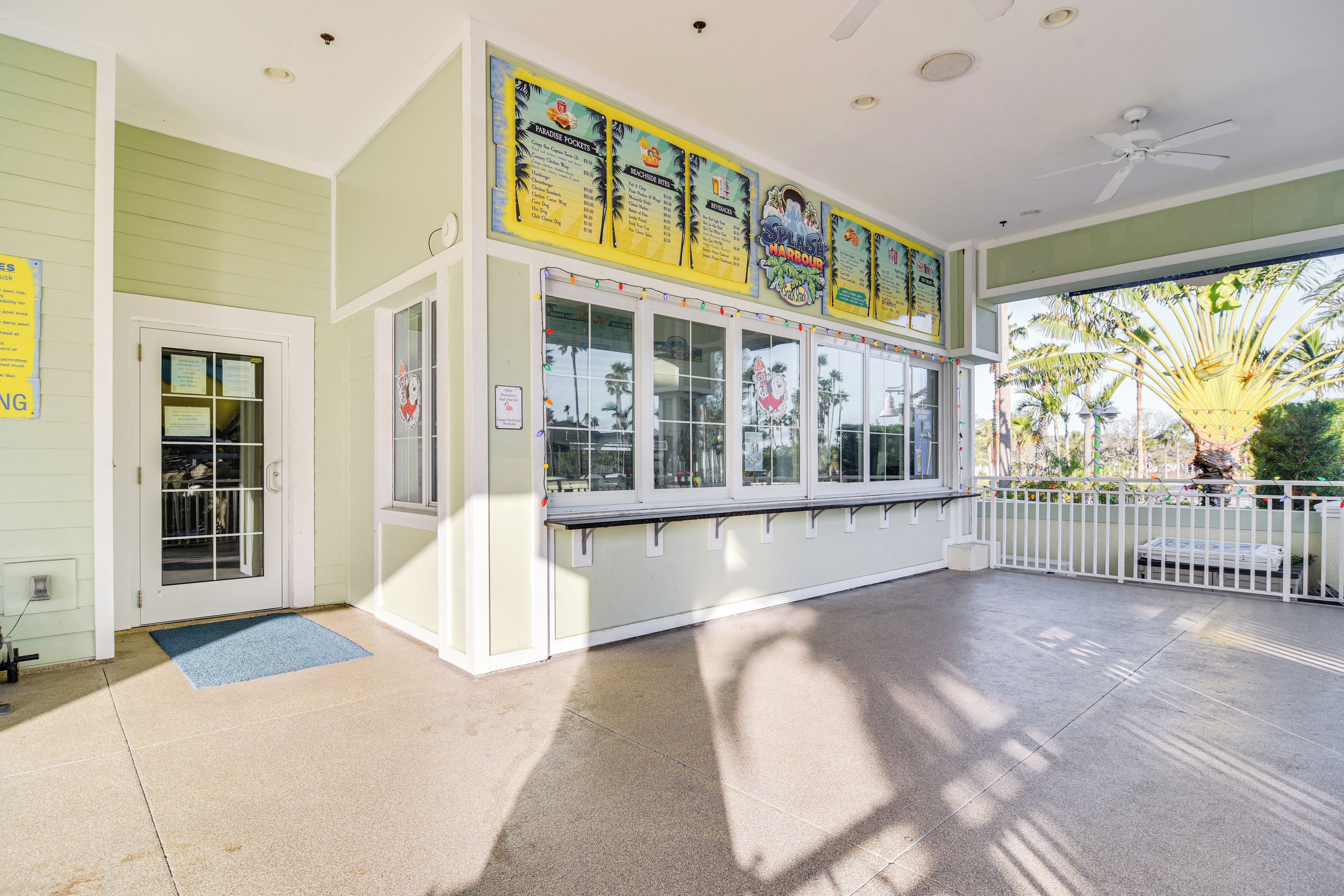 A building with a ticket booth, a blue mat at the entrance, and a white fence.