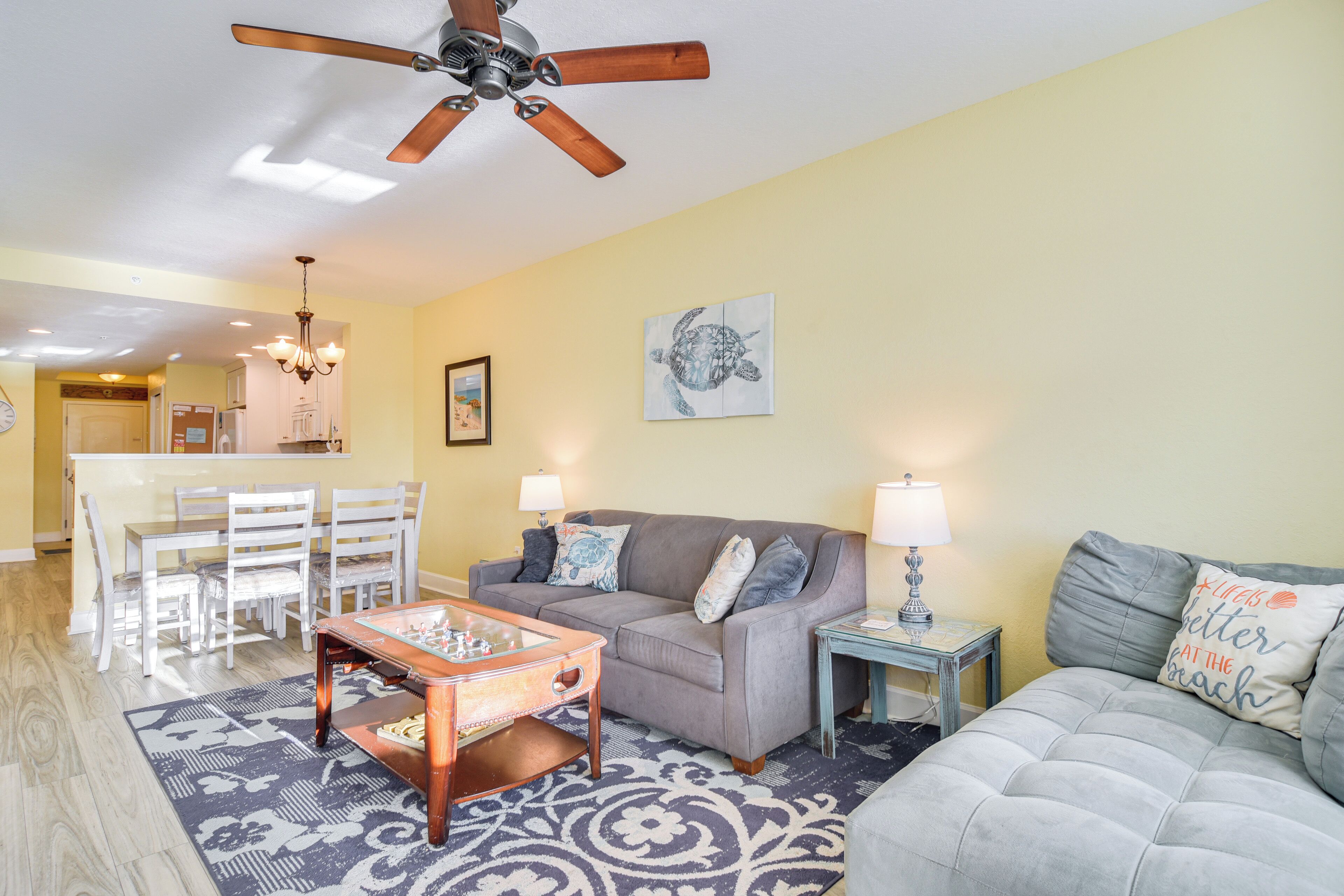 A living room with a gray sofa, a coffee table, and a chandelier. There is a ceiling fan and a painting on the wall.