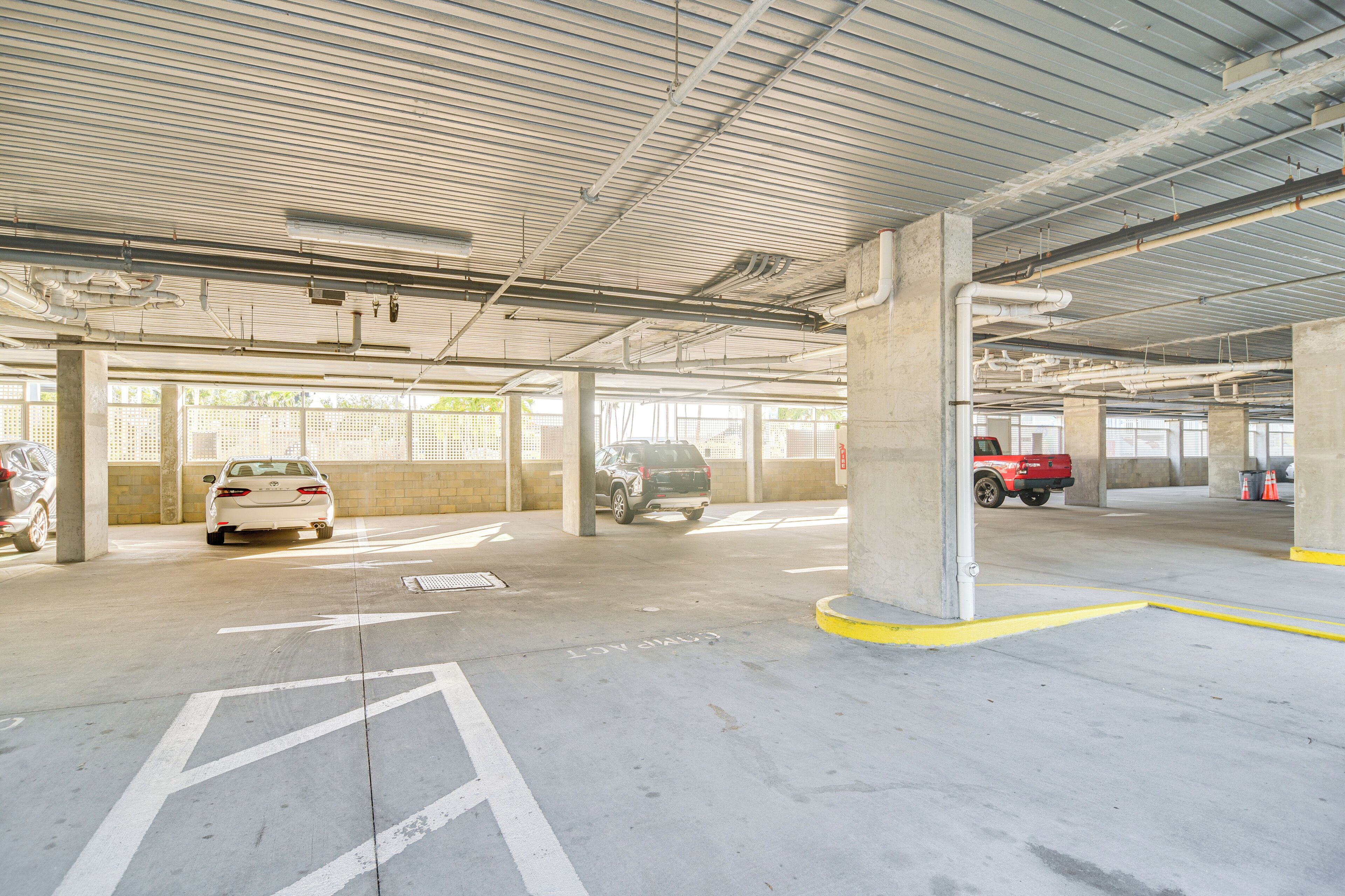 Un estacionamiento de varios niveles con pilares de concreto, espacios demarcados y tuberías elevadas.