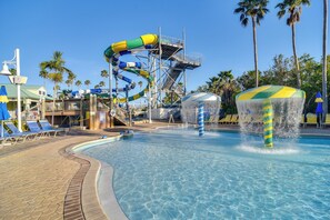 A swimming pool with a water slide, lounge chairs, and palm trees.