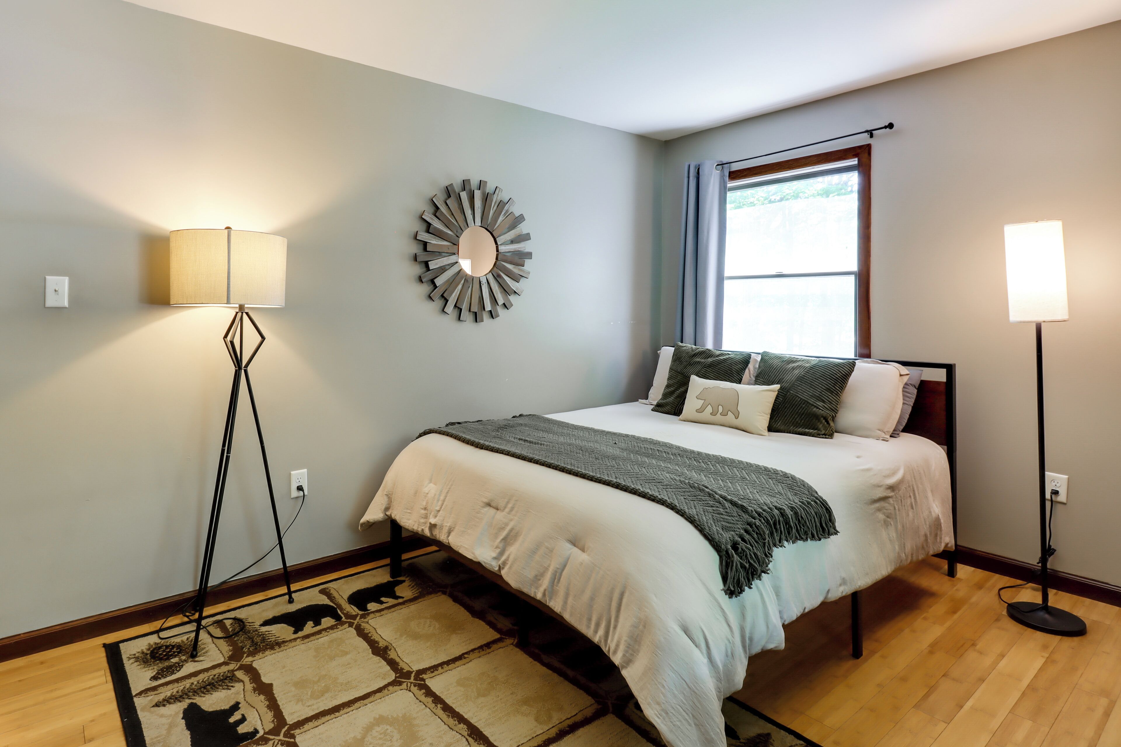 A bedroom with a bed, a floor lamp, a wall mirror, and a window with curtains.