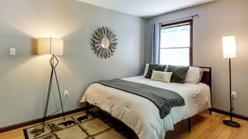 A bedroom with a bed, a floor lamp, a wall mirror, and a window with curtains.