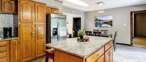A kitchen with wooden cabinets, granite countertops, a stainless steel refrigerator, and a dining area with a table and chairs.