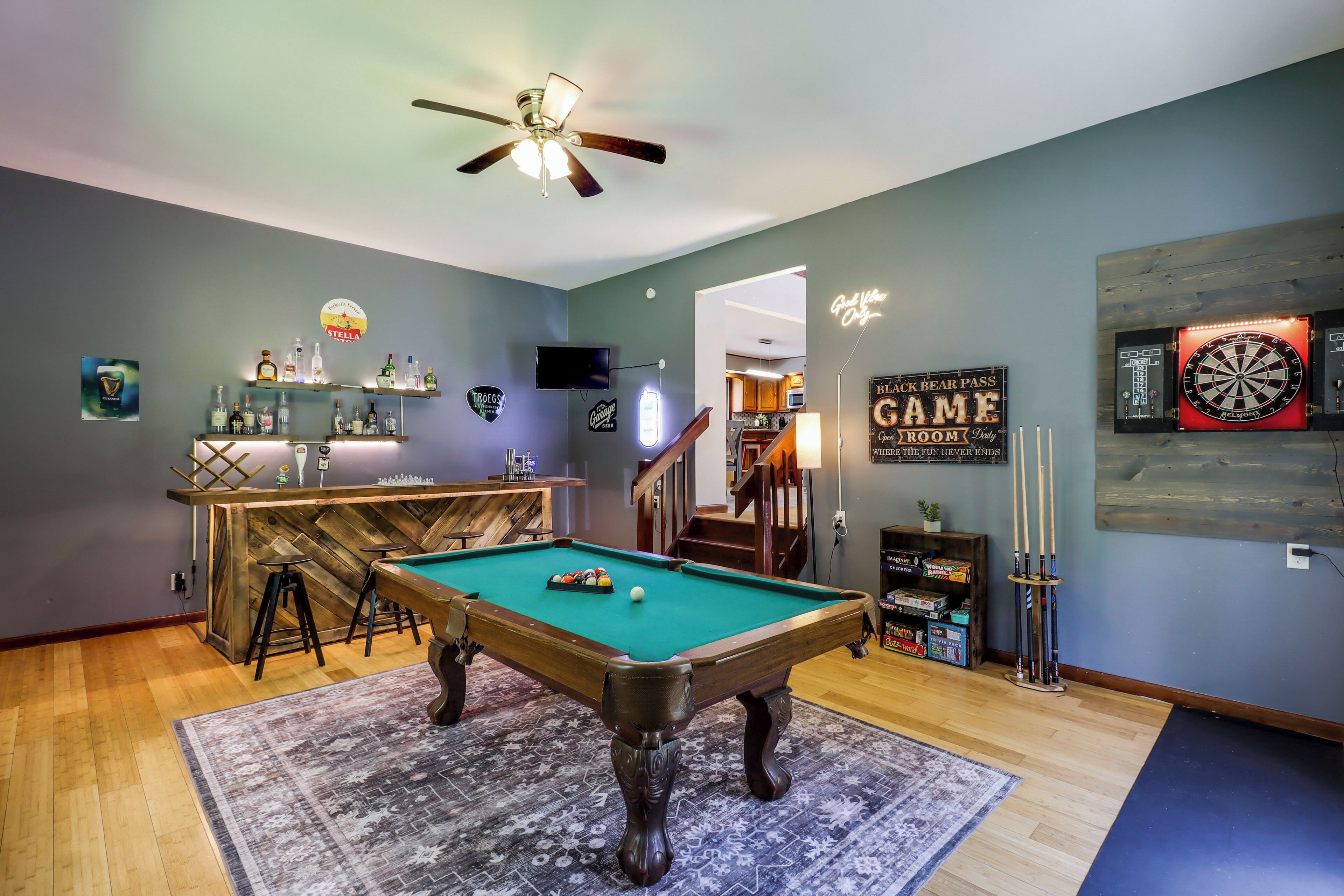 A pool table with a green felt surface, a ceiling fan, and a dartboard.