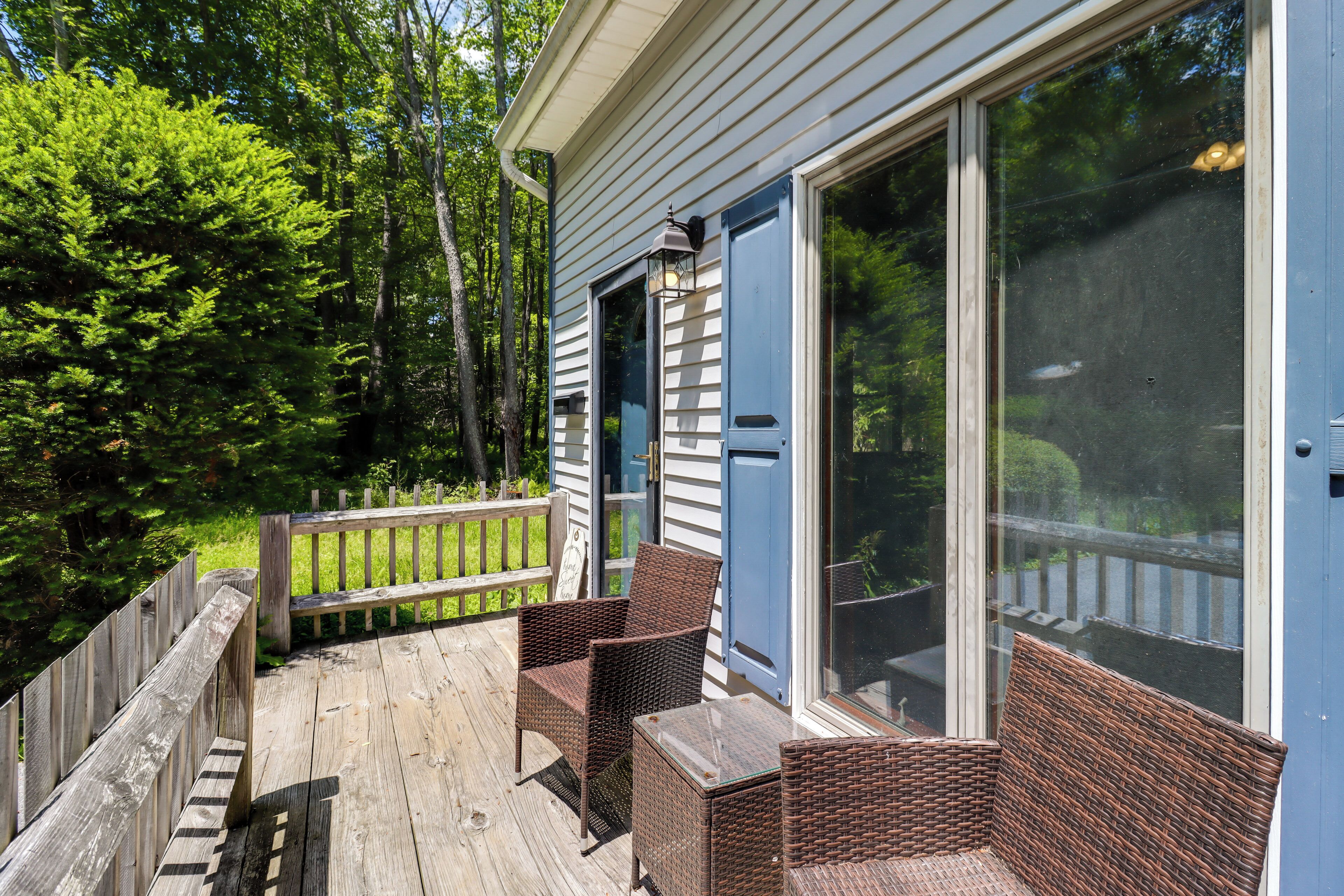 A wooden deck with wicker furniture, a blue door, and a view of trees.