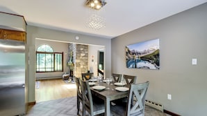 Un comedor con una mesa de madera dispuesta para seis personas, una pared de piedra y un cuadro de un paisaje montañoso.