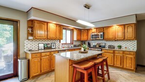 Una cocina con armarios de madera, encimera de granito, microondas de acero inoxidable y un bote de basura.