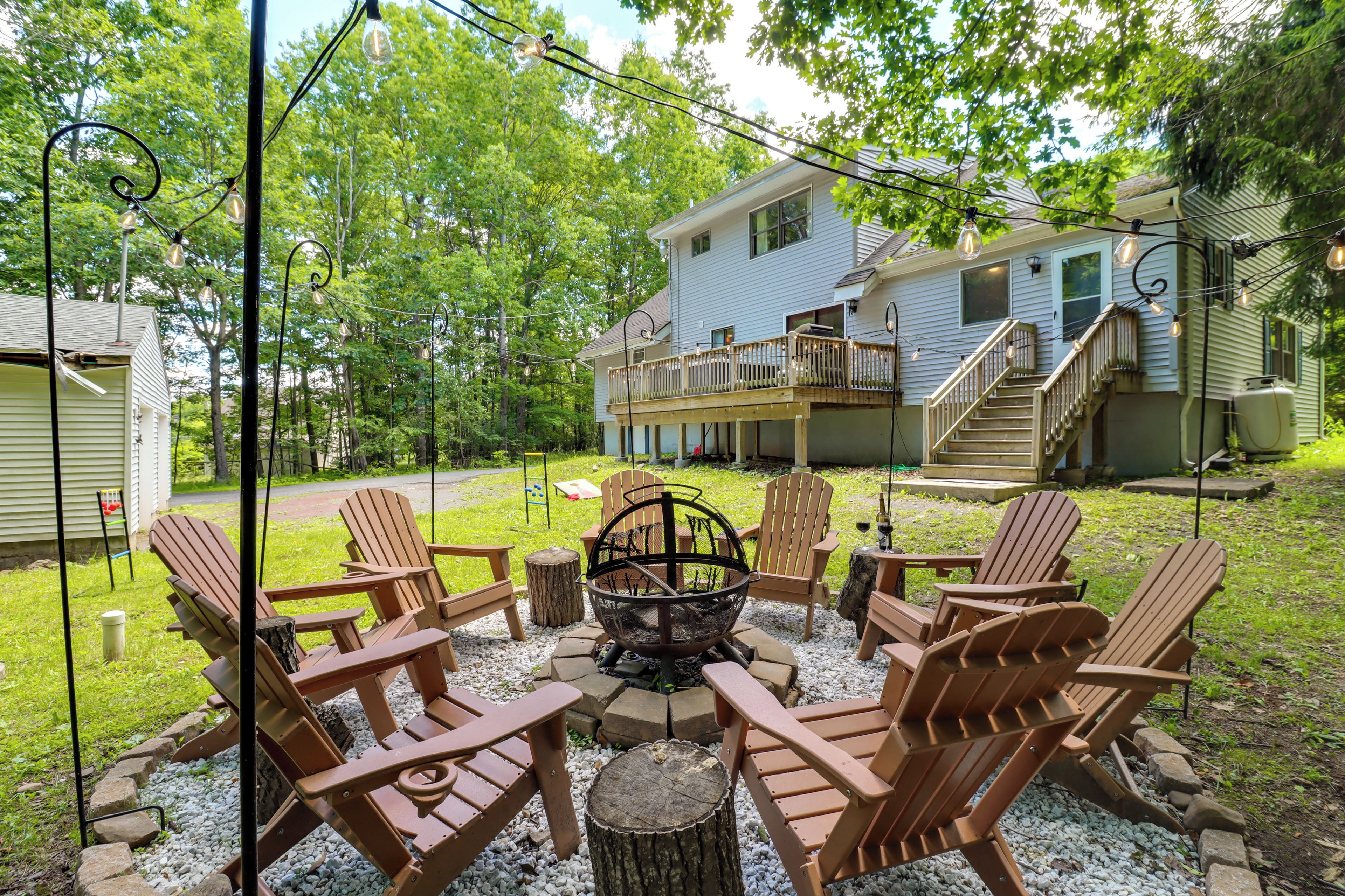 A backyard with Adirondack chairs, a fire pit, and a house with a deck.