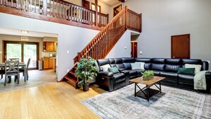 Amplia sala de estar con un sofá de cuero negro, una escalera de madera y un comedor con mesa y sillas.