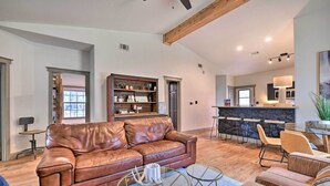 A spacious living room with a leather sofa, coffee table, and striped armchairs. A kitchen area with a stone countertop and bar is visible in the background. - Graford Cabin w/ Rooftop Deck & Lake Views! (Graford)