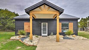 A modern house with a dark exterior, a wooden porch, and a well-maintained front yard with rocks and plants. - Graford Cabin w/ Rooftop Deck & Lake Views! (Graford)