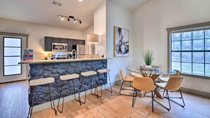 A modern kitchen with a stone island, bar stools, and a dining area with chairs. - Graford Cabin w/ Rooftop Deck & Lake Views! (Graford)