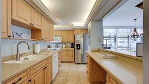 Une cuisine moderne avec des meubles en bois, un réfrigérateur en acier inoxydable, un four à micro-ondes et une grande fenêtre équipée de stores.