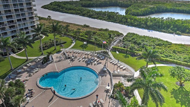 Un hôtel doté d’une grande piscine entourée de chaises longues et de palmiers, offrant une vue sur une plage et l’océan.