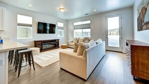 A modern living room with a sofa, a TV, and a dining area with stools. - 12 Mi to Dtwn Flagstaff: Spacious Bellemont Home! (Bellemont)
