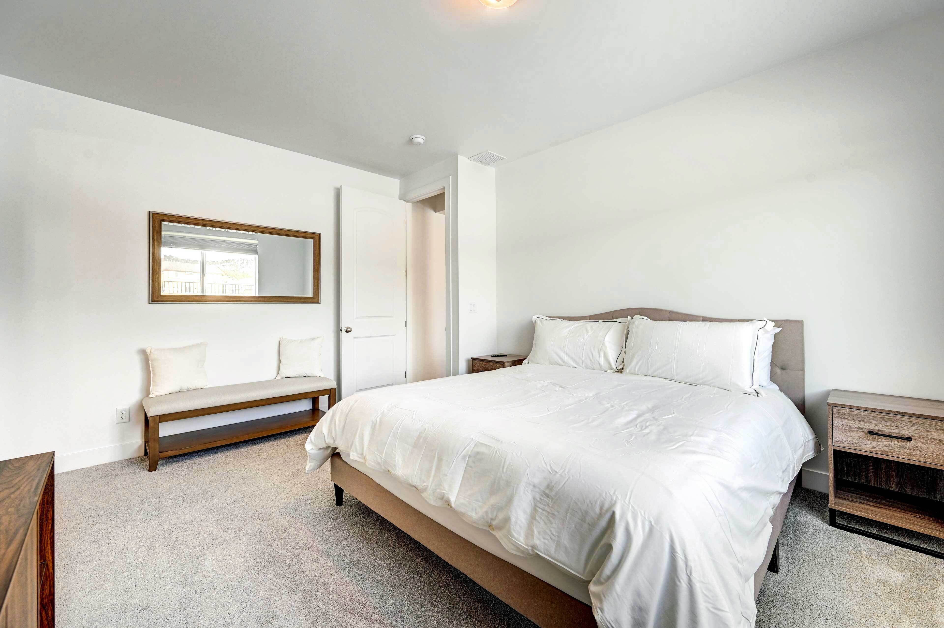 A bedroom with a bed, a bench, a bedside table, and a mirror.