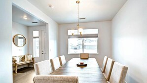 A dining area with a long table, six chairs, a chandelier, a bench with cushions, and a large window with a view of houses. - 12 Mi to Dtwn Flagstaff: Spacious Bellemont Home! (Bellemont)