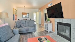 A living room with a grey sofa, a red ottoman, a fireplace, and a ceiling fan. - Mountain-view Tucson Condo w/ Outdoor Pools! (Tucson)